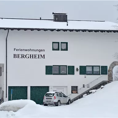 A large, two-story building with the inscription "Holiday Apartments BERGHEIM". The surroundings are covered in snow and have a wintery atmosphere.