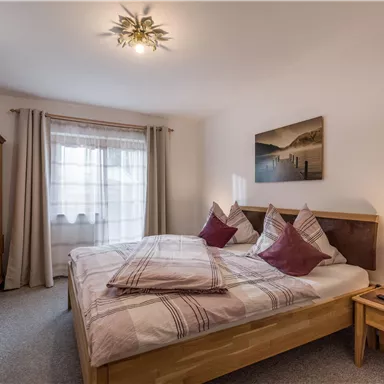 A cozy bedroom with a double bed and decorative pillows. There is a television and a window with curtains that lets in natural light.