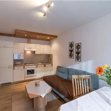 A modern apartment with an open kitchen and a cozy living area. On the table, there is a vase with colorful flowers.