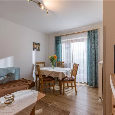 A cozy living space with a table and chairs, surrounded by natural light. Floral decorations create an inviting atmosphere.