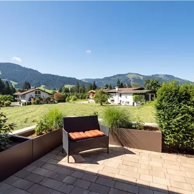 Ein ruhiger Balkon mit Blick auf eine grüne Wiese und Berge im Hintergrund. Eine gemütliche Sitzecke mit einem Kissen lädt zum Entspannen ein.