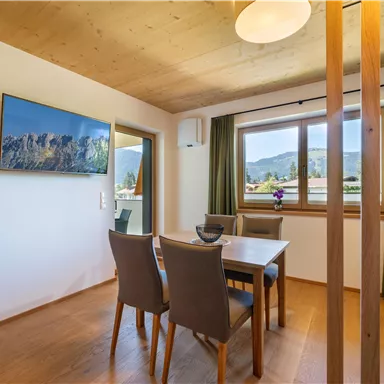 Ein modernes Esszimmer mit einem Tisch und Stühlen. Durch das Fenster sieht man eine schöne Aussicht auf die Berglandschaft.