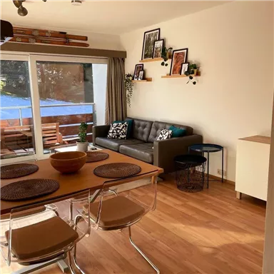 Ein modern eingerichtetes Wohnzimmer mit einer gemütlichen Couch und einem Esstisch. Große Fenster bieten einen Blick auf eine Terrasse mit Gartenmöbeln.