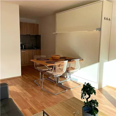 Eine moderne Wohnung mit einem Essbereich und einer offenen Küche. Der Raum ist hell und einladend, mit Holzfußboden und minimalistischer Einrichtung.