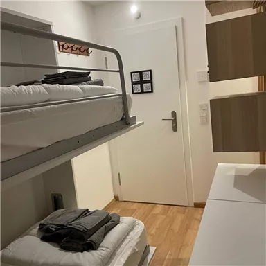 Ein einfaches Zimmer mit einem Hochbett und gestapelten Handtüchern. Die Wände sind hell, und im Raum gibt es einen Schreibtisch und Stuhl.