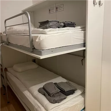 Ein einfaches Schlafraum mit einem Hochbett und einem darunterliegenden Bett. beide Betten sind ordentlich mit Bettwäsche und Handtüchern vorbereitet.