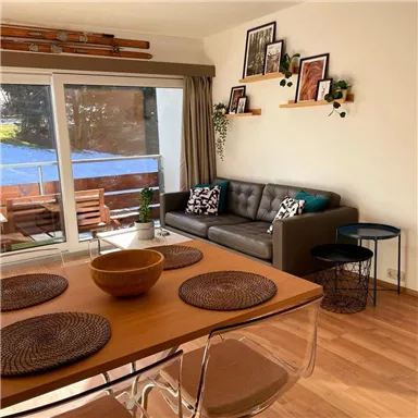 Ein modernes Wohnzimmer mit einem komfortablen Sofa und einem Esstisch. Große Fenster bieten einen Blick auf eine Terrasse mit Gartenmöbeln.