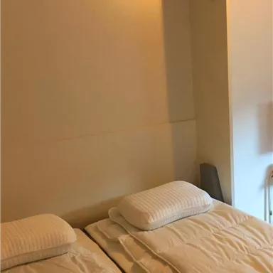 Ein einfaches Zimmer mit zwei Einzelbetten und weißen Bettdecken. Die Wände sind hell und minimalistisch gestaltet.