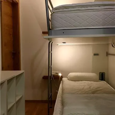 Ein einfaches Schlafzimmer mit einem Etagenbett und einem Schreibtisch. Der Boden ist aus Holz und es gibt einen Kleiderschrank an der Wand.