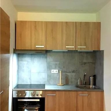 Eine moderne Küche mit Holzschränken und grauen Wänden. Der Herd und die Spüle sind gut angeordnet und der Raum wirkt hell und einladend.