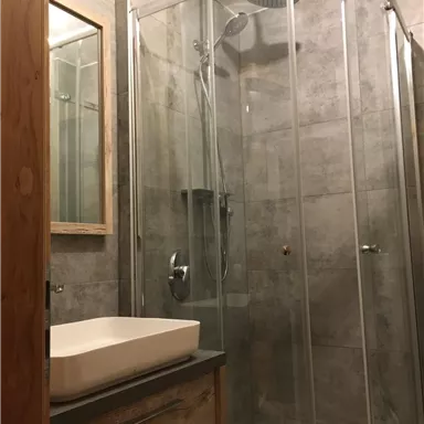 Ein modernes Badezimmer mit einer gläsernen Duschkabine und einer eleganten Waschbeckenanordnung. Die Wände sind mit grauen Fliesen gestaltet, und ein Holzschrank bietet Stauraum.