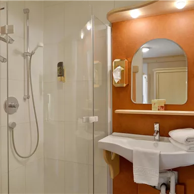 A modern bathroom with a shower cabin and a sink. White towels are neatly stacked on the sink.