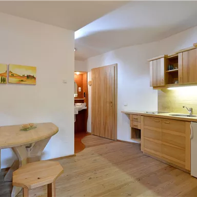 A modern kitchen with wooden cabinets and a dining table. The room is bright and friendly designed.