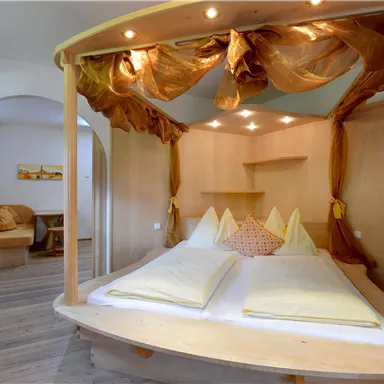 A cozy bedroom with a wooden bed and soft pillows. The warm lighting and decorative curtains create a relaxed atmosphere.