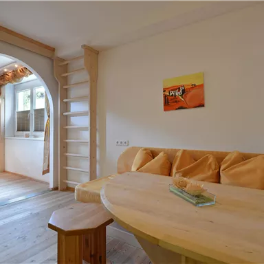 A cozy interior with wooden details and a round seating area. Some pictures hang on the wall, and there is a small staircase in the background.