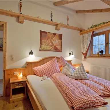 A cozy bedroom with two beds and red checked pillows. The room has wood paneling and large windows that let in plenty of light.