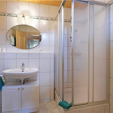 Ein modernes Badezimmer mit einer Duschkabine und einem Waschbecken. Die Wände sind gefliest und mit grünen Handtüchern dekoriert.