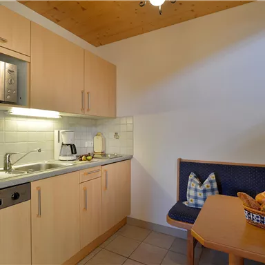 Eine helle Küche mit modernen Geräten und Holzdetails. Ein Tisch mit frischem Obst und einer gemütlichen Sitzgelegenheit ist ebenfalls vorhanden.