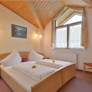 Ein gemütliches Schlafzimmer mit einem Holzdecke und einem großen Fenster. Das Bett ist mit Kissen und Blumen dekoriert.