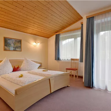 Ein komfortables Schlafzimmer mit zwei Betten und Holzdecke. Große Fenster sorgen für viel Tageslicht und eine gemütliche Atmosphäre.