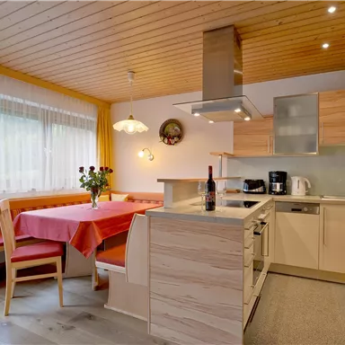 Eine moderne Küche mit Holzverkleidung und hellen Farben. Der Tisch ist mit einer roten Tischdecke gedeckt und es stehen frische Blumen auf dem Tisch.