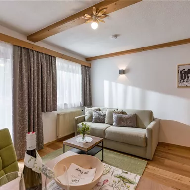 Ein heller Wohnraum mit einem gemütlichen Sofa und einem kleinen Tisch. Große Fenster lassen viel Tageslicht herein.