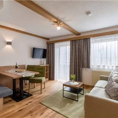 Ein modernes Wohnzimmer mit einem gemütlichen Sofa und einem Esstisch. Große Fenster sorgen für viel Tageslicht und einen einladenden Raum.