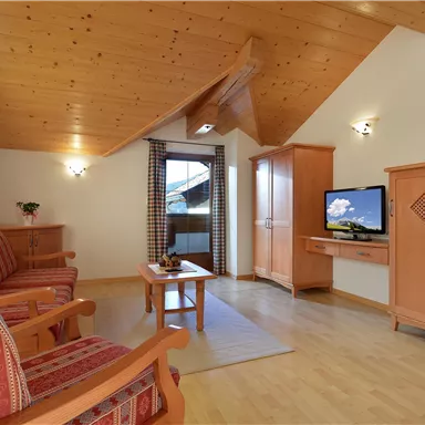 Ein gemütlicher Wohnraum mit Holzdecke und großen Fenstern. Dazu gehören ein Fernseher, ein Sofa und ein Holzmöbelstück.