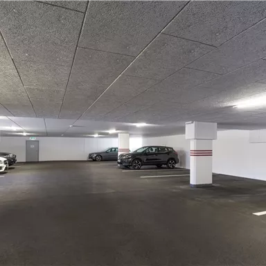 Eine moderne Tiefgarage mit mehreren abgestellten Autos. Der Raum ist gut beleuchtet und hat einen klaren, strukturierten Boden.