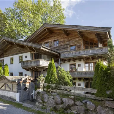 A traditional alpine house with wooden cladding and spacious balconies. Surrounded by green trees and a well-maintained garden.