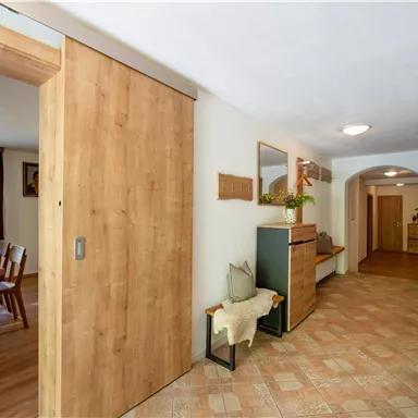Ein heller Flur mit Holzdetails und einem einladenden Ambiente. Auf der linken Seite befindet sich ein Esstisch und rechts eine Garderobe.