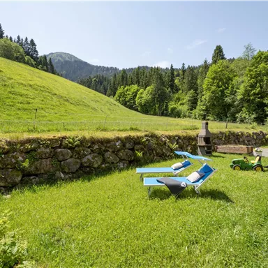 Eine schöne Wiese mit zwei Liegen und einer kleinen grünen Fahrzeug. Im Hintergrund sieht man einen bewaldeten Hang und einen blauen Himmel.