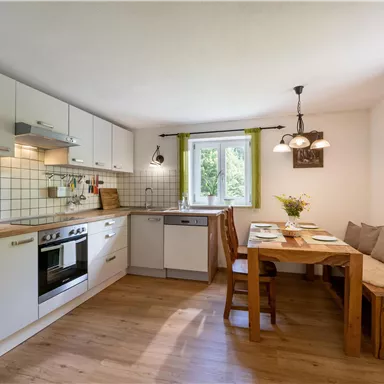 Eine moderne Küche mit weißen Schränken und Holzfußboden. Ein Essbereich mit einem Holztisch und bequemen Sitzgelegenheiten ist ebenfalls vorhanden.