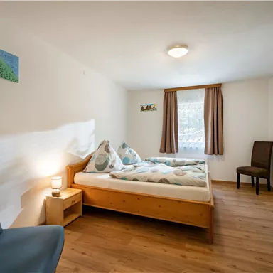 Ein gemütliches Zimmer mit zwei Einzelbetten und einem bequemen Sessel. Das Zimmer hat helle Wände, einen Holzfußboden und eine ruhige Atmosphäre.