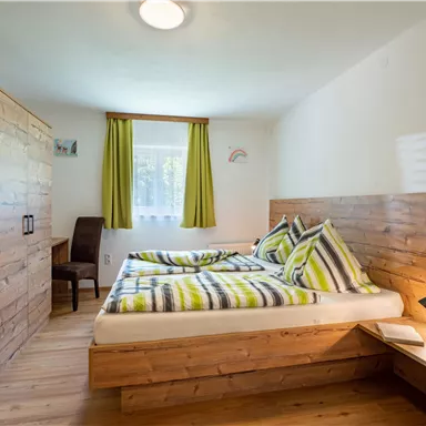 Ein gemütliches Schlafzimmer mit einem Doppelbett und Holzverkleidungen. Die Fenster sind mit grünen Vorhängen geschmückt und es gibt einen Schreibtisch in der Ecke.