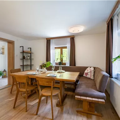 Ein gemütlicher Essbereich mit einem großen Holztisch und Sitzgelegenheiten. Durch große Fenster fällt natürliches Licht in den Raum.