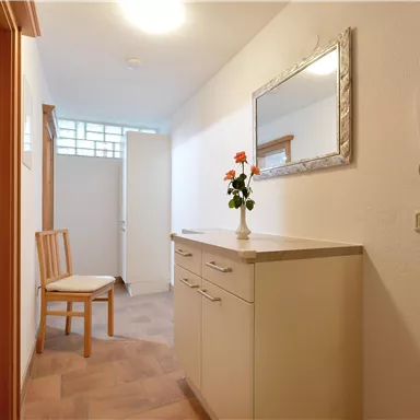 A bright hallway with a white dresser and a mirror cabinet. A chair and a small bouquet create an inviting atmosphere.