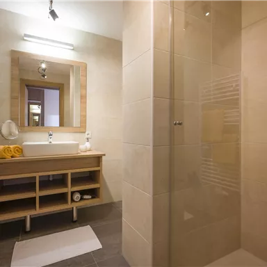 A modern bathroom with a shower and a sink. The soft colors and the wooden details create an inviting atmosphere.