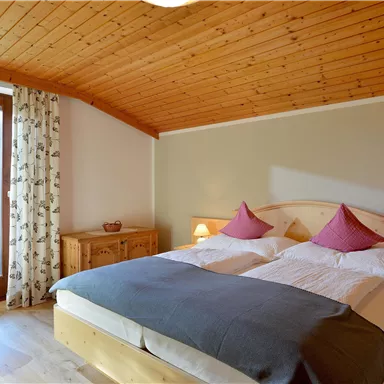 A cozy bedroom with two single beds and pink pillows. The wooden walls and the large balcony create a warm atmosphere.