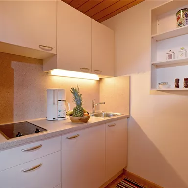 A small, modern kitchen with bright cabinets and a sink. On the windowsill, there is a pineapple and there is a decorative shelf above it.