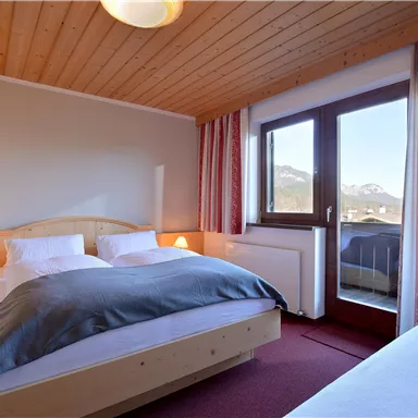 A cozy bedroom with a double bed and an additional single bed. Large windows offer a view of the mountains and plenty of daylight.