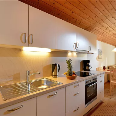 A modern kitchen with white cabinets and a wooden ceiling. Chairs are around the table and a cozy atmosphere prevails.