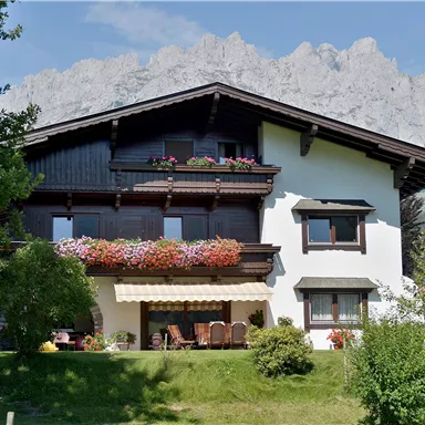 A beautiful house with blooming balcony flowers and a large garden. Impressive mountains can be seen in the background.