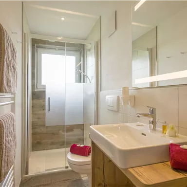 A modern bathroom with a shower and a wooden sink. Ears made of towels and a red washcloth add a decorative touch.