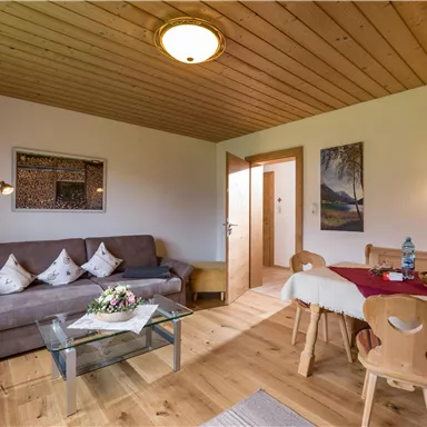 A cozy living room with a sofa, a table, and wooden furniture. The warm colors and the wooden ceiling create an inviting atmosphere.