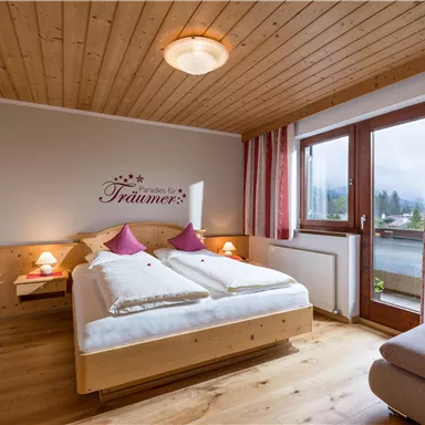 A cozy bedroom with wooden paneling and a double bed. The windows offer a view outside, and the decor radiates tranquility.