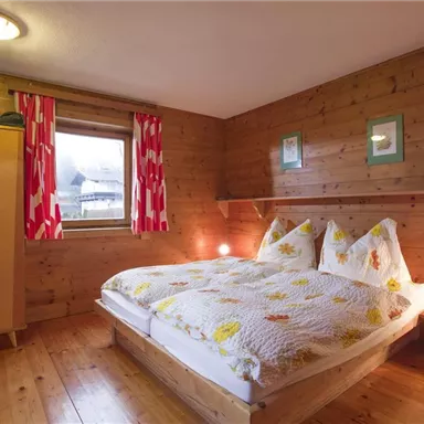 A cozy bedroom with wooden paneling. There is a double bed, a wardrobe, and colorful curtains.
