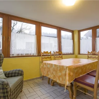 A cozy dining area with a large table and chairs. The walls are painted yellow, and the windows let in a lot of light.