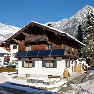 A beautiful chalet in the mountains, surrounded by snow. In the background, majestic mountains rise under a clear blue sky.