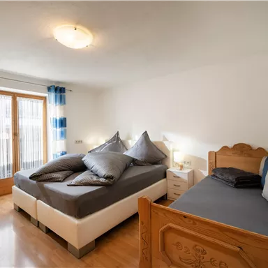 A bright bedroom with a double bed and a single bed. Large windows let in plenty of light, and the walls are painted in neutral colors.